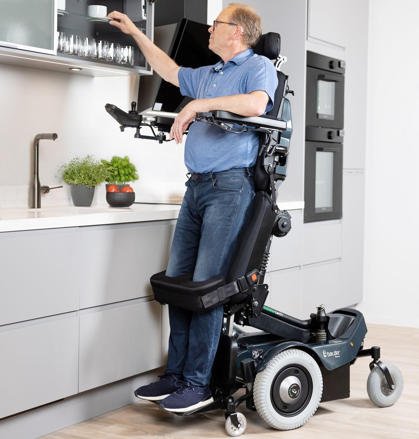 A white male using a Balder F390 standing powerchair. He is in the standing position and reaching into a high cupboard.